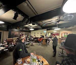 A group of people wearing costume hats seated around tables in a room.