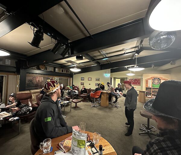 A group of people wearing costume hats seated around tables in a room.