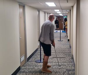 Four men are playing mini-golf on a makeshift course in a hallway with closed doors on each side
