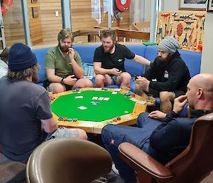 Six men are sitting around a card table playing poker