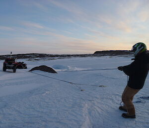 A man is pulling a quad-bike using a rope, pulley, and anchors drilled into the ice