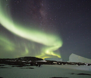 A bright green aurora is in the sky above two ice-bergs and a rocky island.