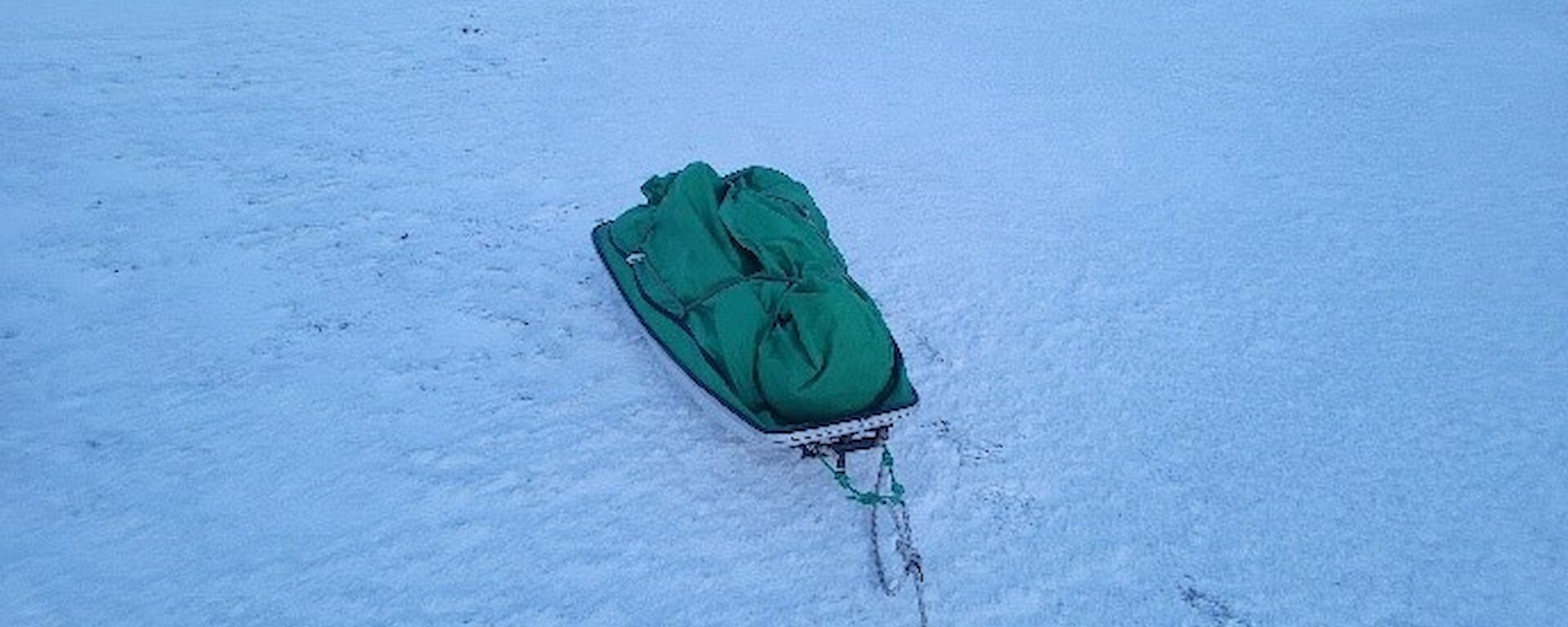 A simple sled containing equipment under green cover sits on the sea-ice.