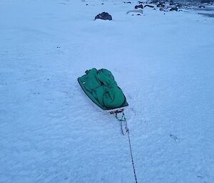 A simple sled containing equipment under green cover sits on the sea-ice.