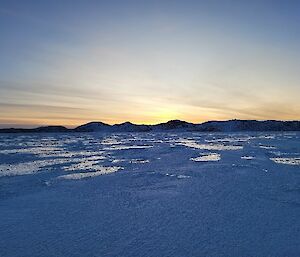 Looking over sea-ice to hills in the distance. The light has the gentle hues of sunset.