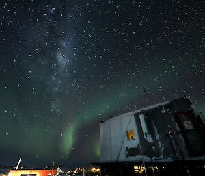 A green aurora and the Milky Way galaxy can be seen in the night sky above an older, raised building.