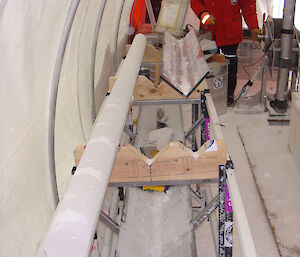 An ice core sitting on a processing table inside a tent, with a man standing beside an ice core drill.