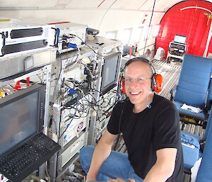 A man sitting beside computer equipment inside an aircraft.