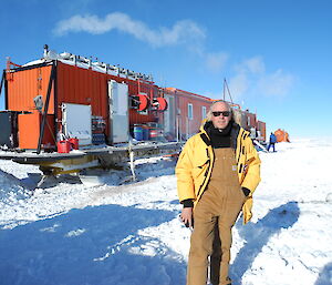 A man stading in front of a traverse consisting of shipping containers on sleds, in Antarctica.