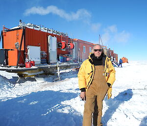A man standing in front of a traverse consisting of shipping containers on sleds, in Antarctica.