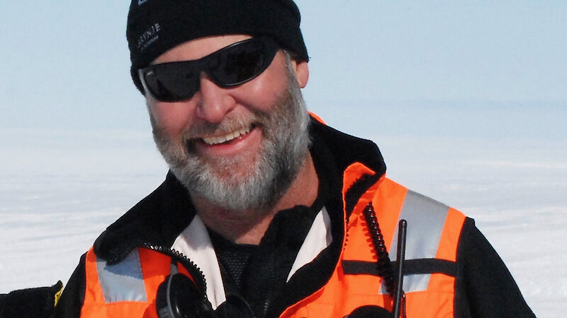 A man in an orange high vis vest and black beanie in Antarctica.