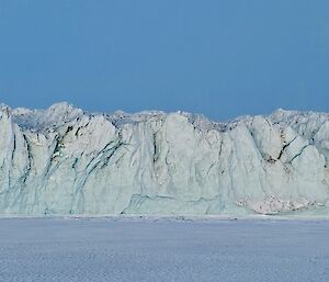 A clsoe up of the edge of a glacier in various shades of light blue, white and grey showing many cracks and crevices.