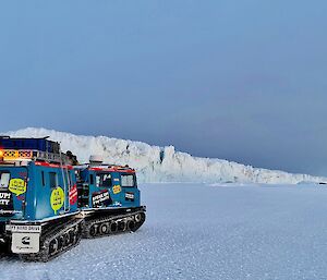 A Blue Hägglunds on the sea-ice in the foreground set against the side wall of a white cracked and creviced glacier.