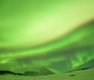 An Aurora covers the entire sky over an ice covered shore with two icebergs in the middle of frame.