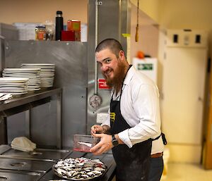 A smiling man in waiter clothes applies garnish to two trays of oysters