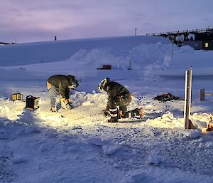 Two men are cutting sea ice to prepare a swimming hole