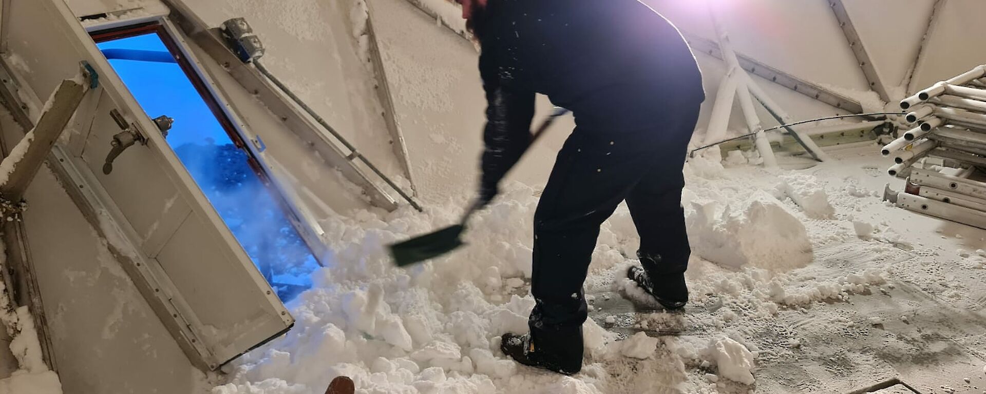 A man is inside a dome shape building and shovelling snow from the inside out the door