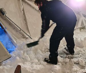 A man is inside a dome shape building and shovelling snow from the inside out the door