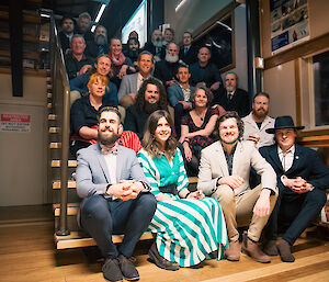 A group of smiling, well-dressed people sitting on stairs for a team photo.