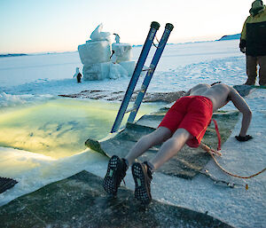 A man in red board shorts does push-ups next to the swimming hole cut into the sea-ice.