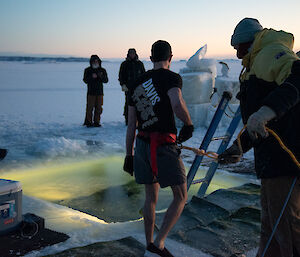 An expeditioner wearing a black t-shirt with "Davis" printed on the back prepares for his icy plunge into the swimming hole.