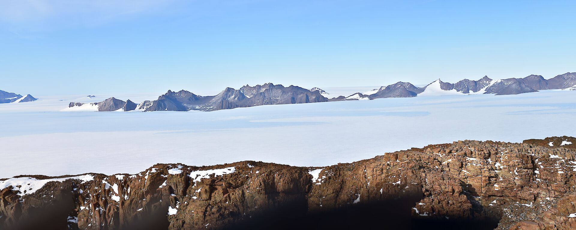 In the foreground and in the far distance are rocky mountain peaks separated by an expanse of ice