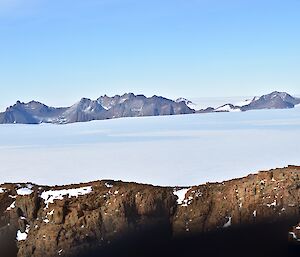 In the foreground and in the far distance are rocky mountain peaks separated by an expanse of ice