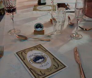 A table setting is ready for a formal dinnerr with a menu in the centre of the place