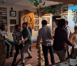 A group of people are in a bar area dancing and laughing. A game of giant jenga is being played in the middle of scene.