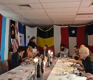Two women and ten men are around a large table talking and laughing. Flags are hanging in the background all around the table.