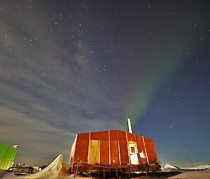A red building is in the centre of frame with stars and a green and purple aurora visible in the sky above