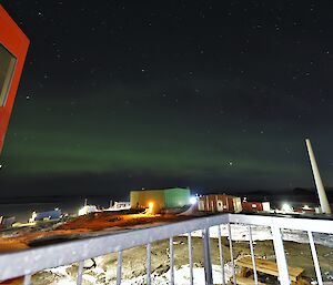 A green aurora is visible in the sky above multicoloured buildings on a rocky landscape