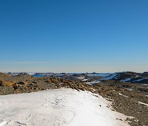 A landscape photo with a snow covered foreground, and rocky low hills in the background. leading further on to a clear blue sky.