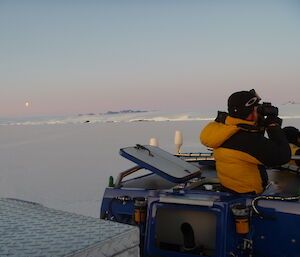 Two men are standing in the cupola of a blue Hägglunds vehicle looking through binoculars into the distance