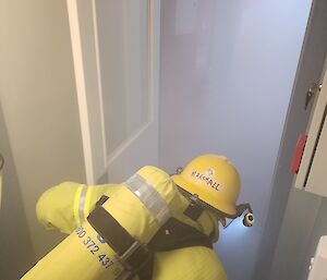 A man wearing a fire-fighting outfit including helmet and breathing apparatus enters a smoke filled room.