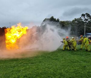 A group of people wearing firefighter's outfits use a hose to fights a large gas fire at the fire training centre.