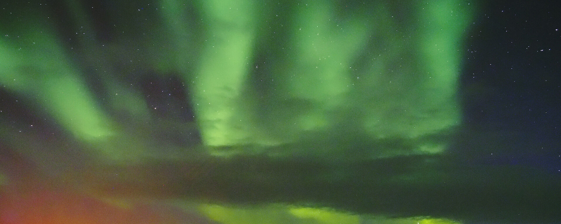 A bright green Aurora is visible in the night sky above icebergs and rocky islands. It appears to make the shape of a hand.