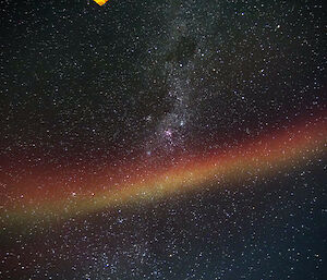 A red Aurora stretches across the night sky with the Milky Way visible behind it.