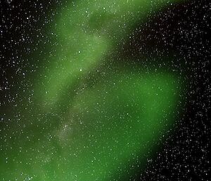 A green Aurora stretches across the night sky with the Milky Way visible behind it.