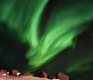 A bright green aurora is visible in the night sky above a rocky, snow covered landscape.