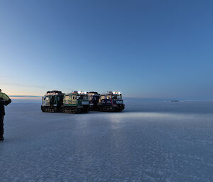 A man is walking over the sea-ice with two Hägglunds vehicles in the background