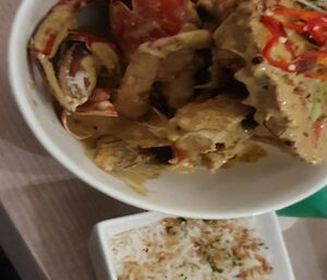 A bowl containing cooked  chilli mud crabs and another bowl next to it containing rice and seasoning