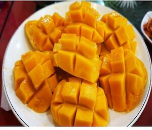 A white plate containing six freshly cut mango cheeks