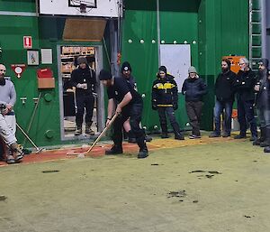 A man is about to take a shot with a hockey stick and a puck made of ice. There are nine people watching on.