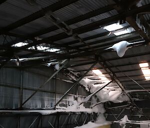 Snow has built up in the trusses inside an old metal hangar building