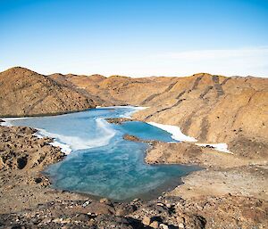 A vivid blue frozen lake surrounded by rocky hills