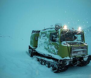 A green Antarctic field truck drives through a snow-covered landscape.
