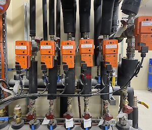 A line of six orange electrical boxes across a wall, with insulated pipes coming from the top and bottom of them.
