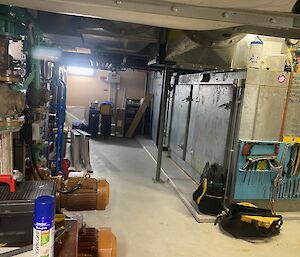 A large silver metal air conditioning unit sits in a concrete floored utility room.