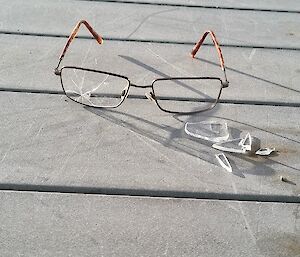 A set of broken reading glasses with the glass from one eye completely broken into pieces sitting in front of the glasses frame...